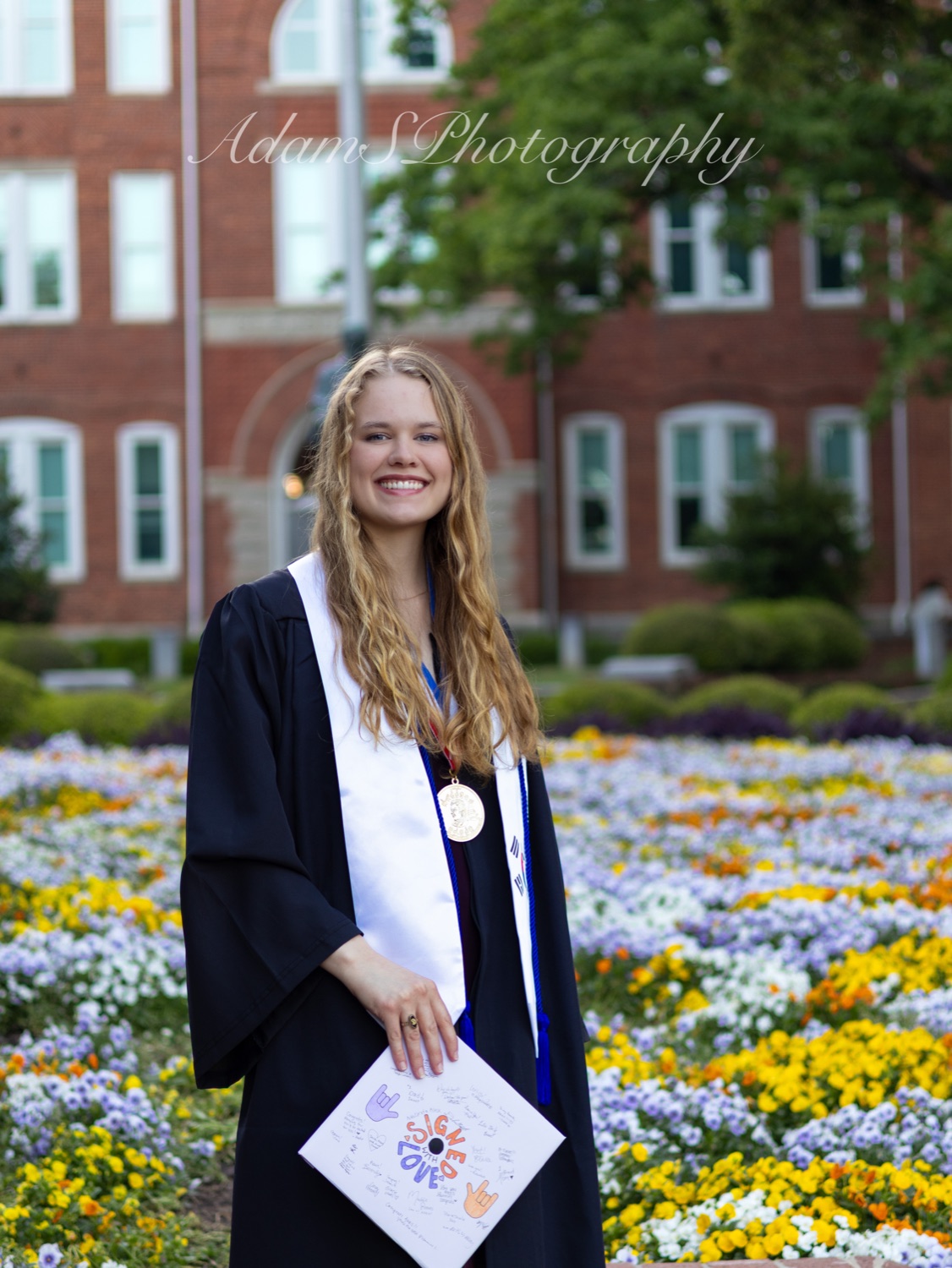 Graduate in cap and gown standing in a flower garden at Clemson